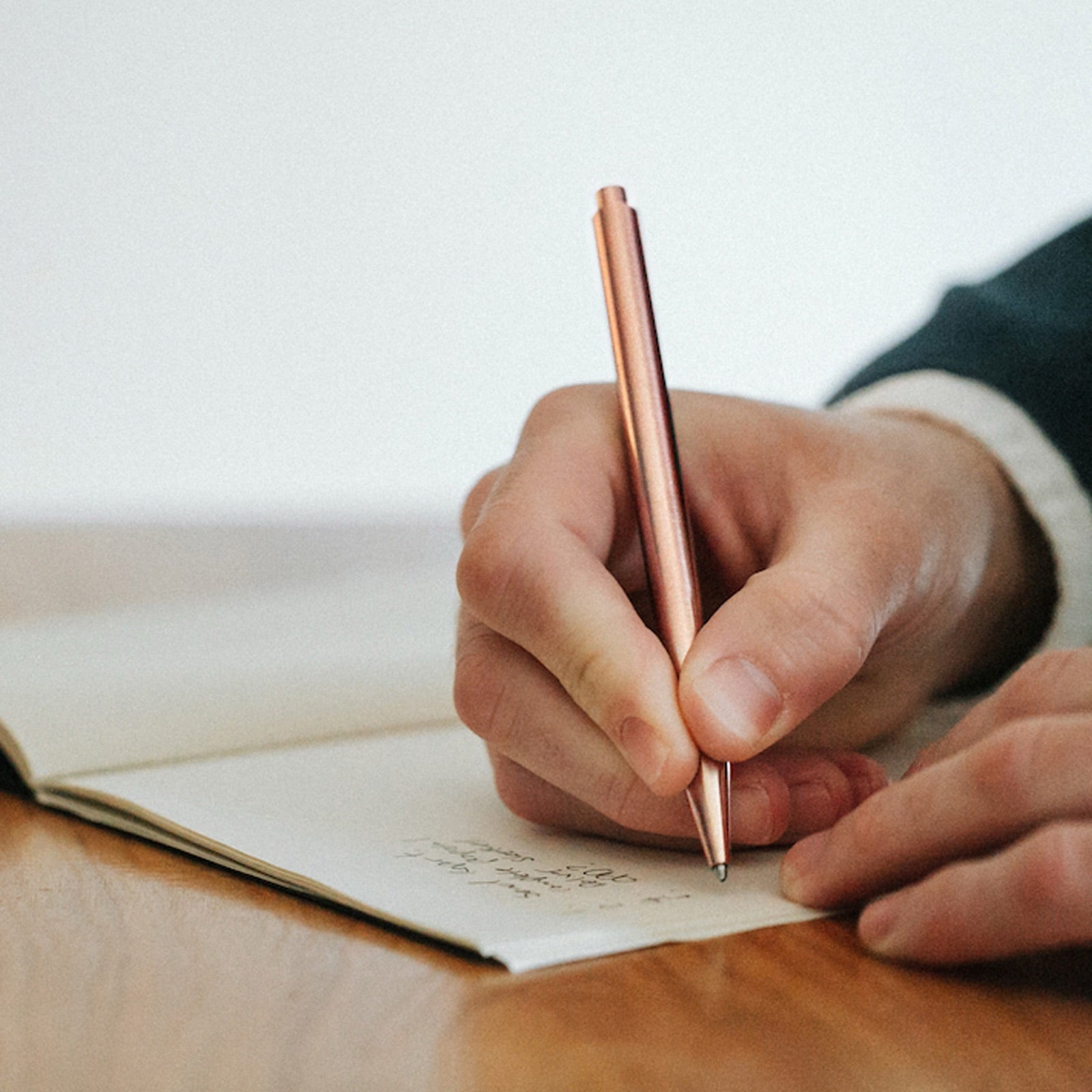 A man writing in a notebook with a copper Modern Fuel pen
